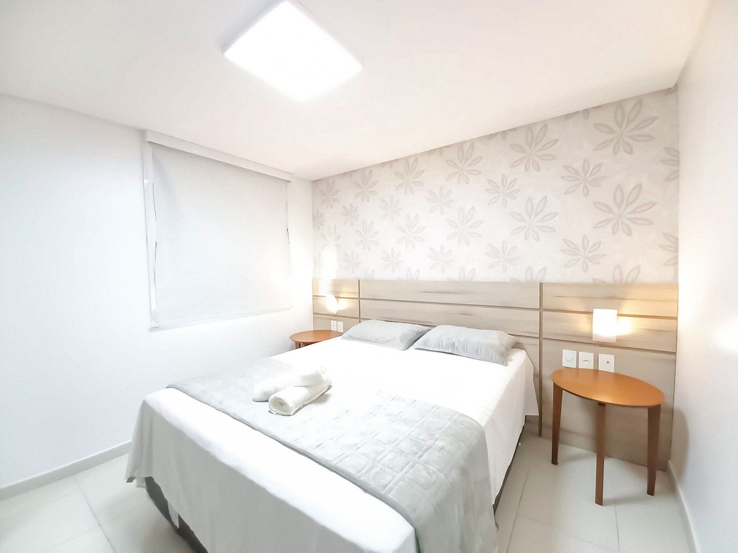 A modern hotel room with a large bed, two bedside tables, a headboard with integrated lighting, and a floral-patterned wall.