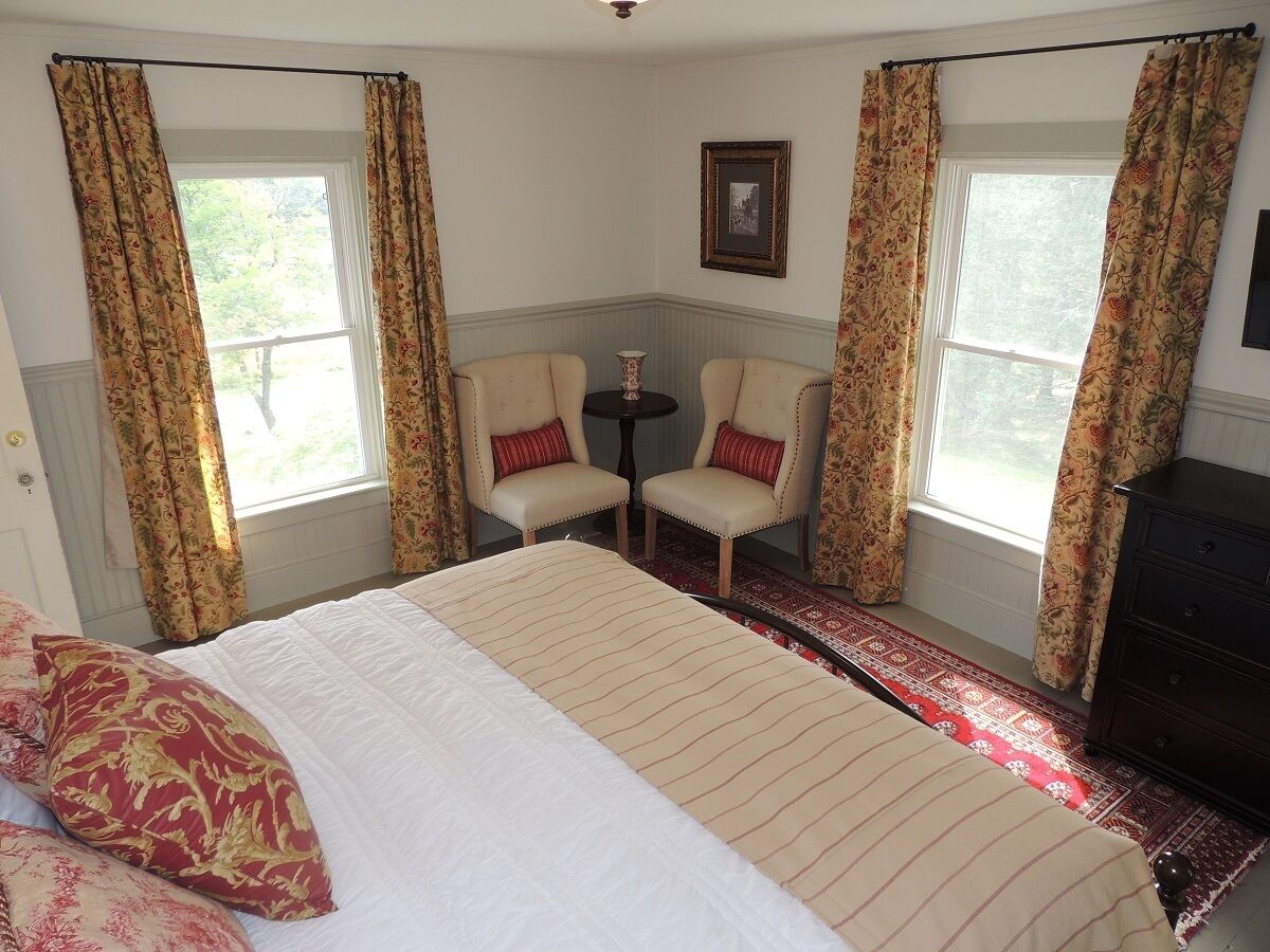 A bedroom with a large bed, two chairs, a small table, and a dresser.