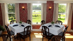 Comedor con una mesa preparada para cuatro, ventanas grandes con cortinas y vistas a un paisaje verde.