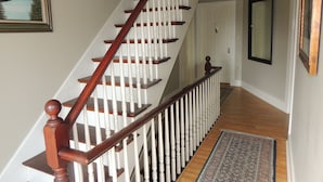 Una escalera con escalones de madera y barandillas blancas que lleva a una puerta, con un espejo y un cuadro en la pared.