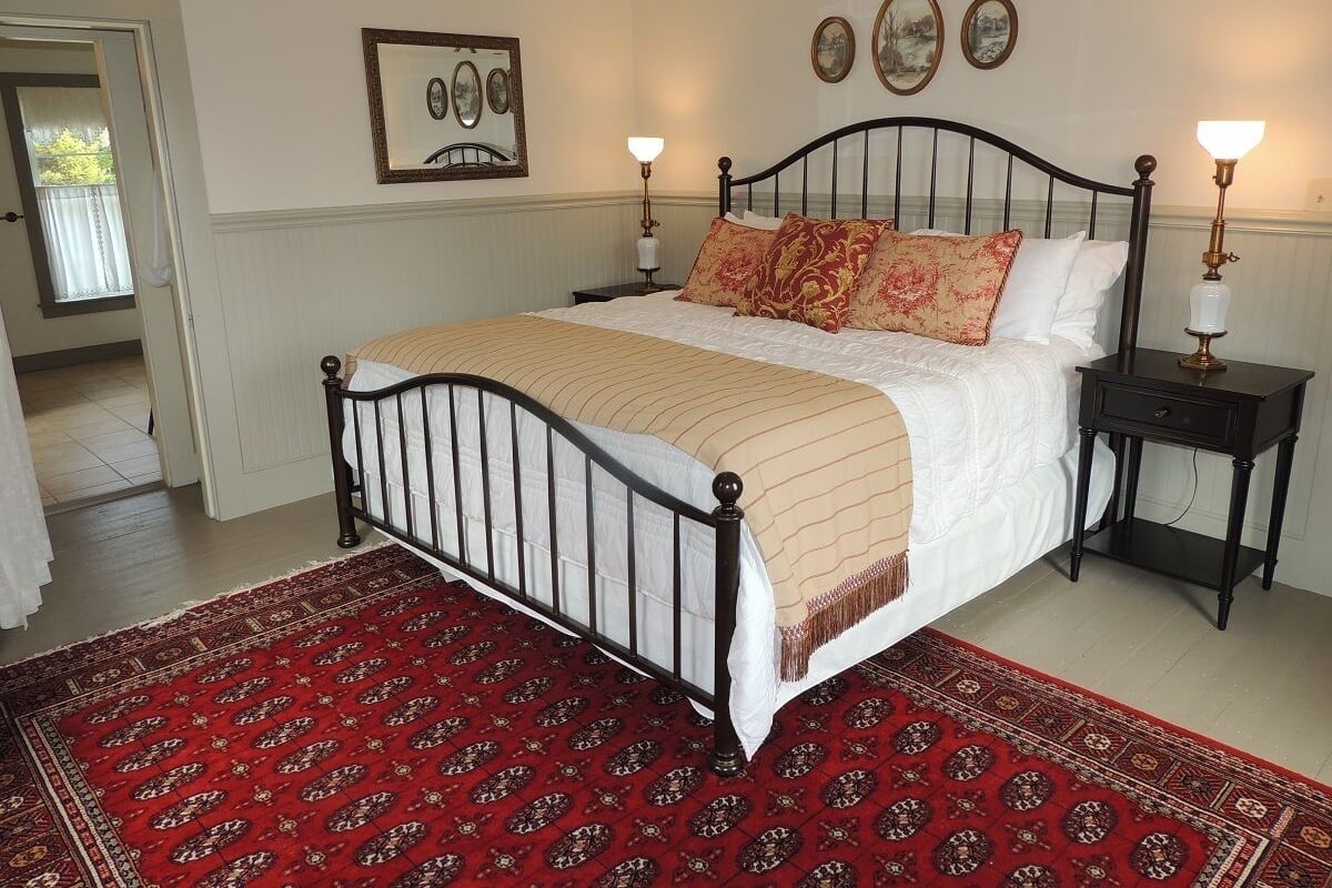 A bedroom with a bed, two bedside tables, a red patterned rug, and wall-mounted artwork.