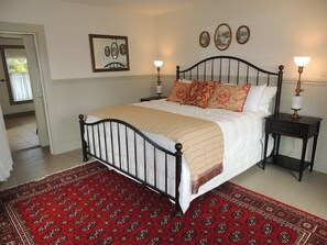 Une chambre à coucher comprenant un lit, deux tables de chevet, un tapis rouge à motifs et des œuvres d’art accrochées au mur.