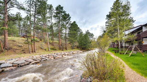 A river flowing through a forested area with a building on the right side. - Estes Park Condo Rental: Balcony w/ River Views! (Estes Park)