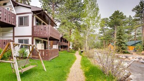 A two-story building with a gravel path leading to a wooden swing set. - Estes Park Condo Rental: Balcony w/ River Views! (Estes Park)