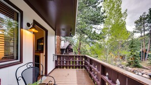 A wooden deck with a railing, a table with a cheese platter, and a chair. - Estes Park Condo Rental: Balcony w/ River Views! (Estes Park)