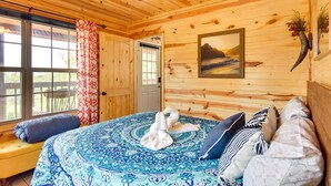 Ein Zimmer in einer Holzhütte mit einem Bett, einer Bank und einem großen Fenster.
