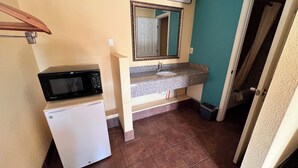 Une petite salle de bain avec un réfrigérateur blanc, un four à micro-ondes noir, un évier doté d’un plan de travail en granit et un miroir au-dessus de l’évier.