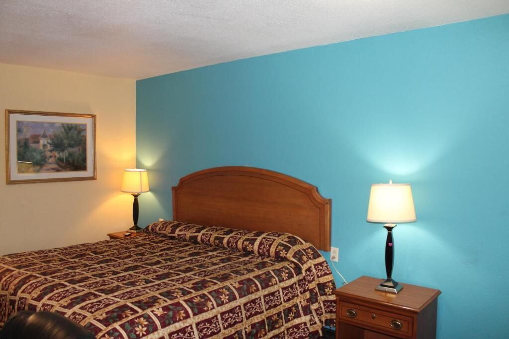 A bedroom with a wooden headboard, a patterned bedspread, two bedside lamps, and a framed picture on the wall.