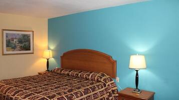 A bedroom with a wooden headboard, a patterned bedspread, two bedside lamps, and a framed picture on the wall.