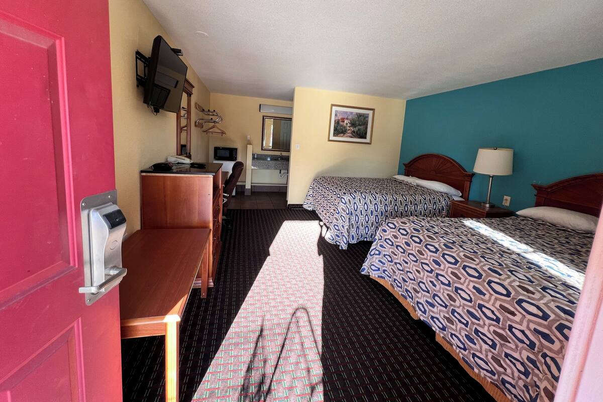 A hotel room with two beds, a desk, a chair, a microwave, a sink, and a mirror.