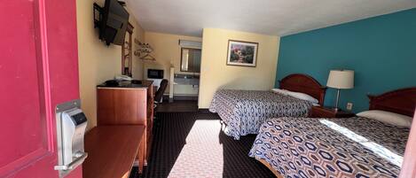 A hotel room with two beds, a desk, a chair, a microwave, a sink, and a mirror.
