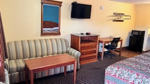Une chambre d’hôtel avec un canapé à rayures, une petite table en bois, un bureau avec une chaise, une télévision, une horloge et un four à micro-ondes.