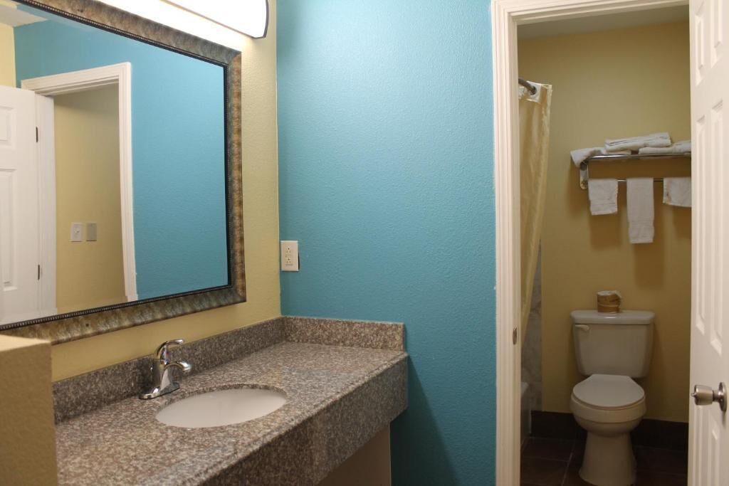 Un baño con lavamanos de encimera de granito, un espejo, inodoro y toallero.