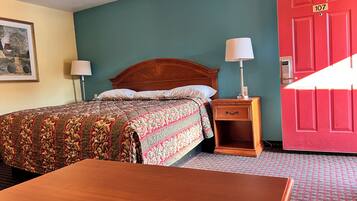 A hotel room with a bed, nightstand, lamp, and a red door with the number 107.