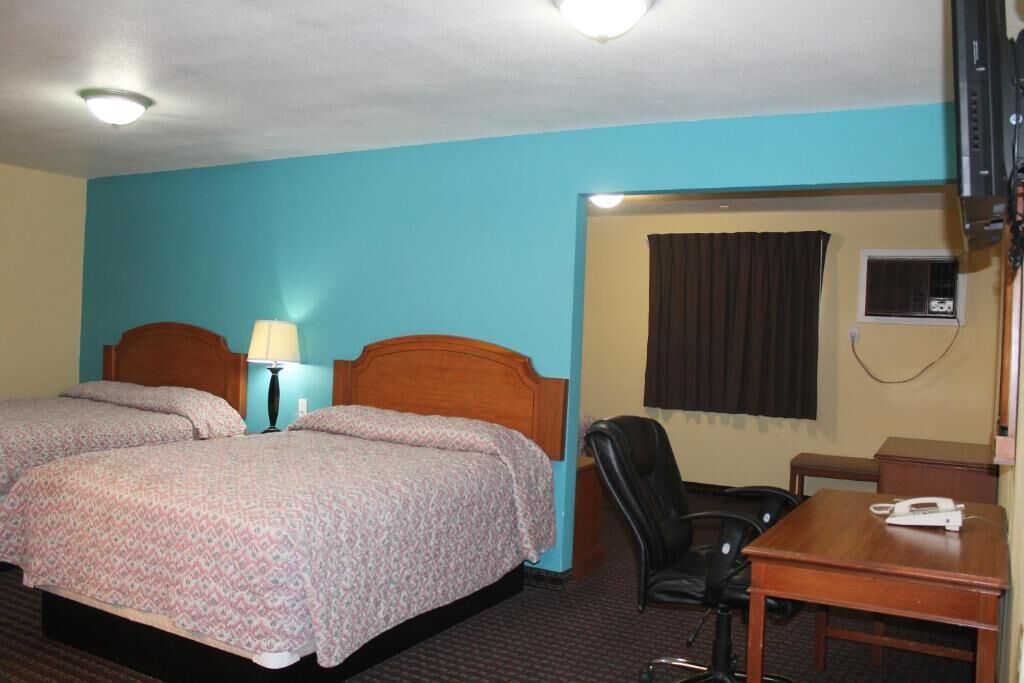 Habitación de hotel con dos camas, un escritorio, una silla y una ventana con cortinas.