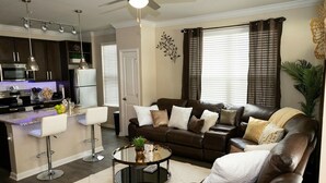 A modern living room with a brown leather sofa, a round coffee table, and a kitchen area with dark cabinets and a white refrigerator. - Cozy Luxury Midtown 1 Bedroom Condo  (Atlanta)