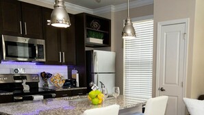 A kitchen with dark cabinets, stainless steel appliances, a granite countertop, and two white bar stools. - Cozy Luxury Midtown 1 Bedroom Condo  (Atlanta)