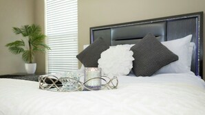A neatly made bed with a white comforter, a decorative metal tray, and a glass candle holder. - Cozy Luxury Midtown 1 Bedroom Condo  (Atlanta)