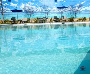 Une piscine aux eaux cristallines, bordée de chaises longues et d’ombrelles, entourée d’arbres et offrant une vue sur l’océan.