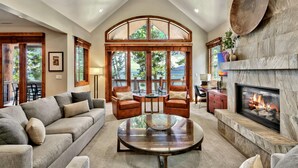 A spacious living room with a fireplace, a large window overlooking a deck, and a cozy seating area. - 8 Sierra Shores - Stunning Lakefront 4BR/4BA (South Lake Tahoe)