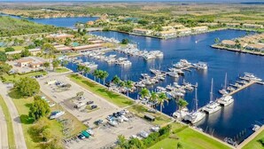 An aerial view of a marina with multiple docks and boats, surrounded by greenery and buildings.