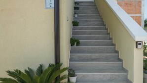 A staircase leading to a door with a sign above it. There are potted plants at the base of the stairs.