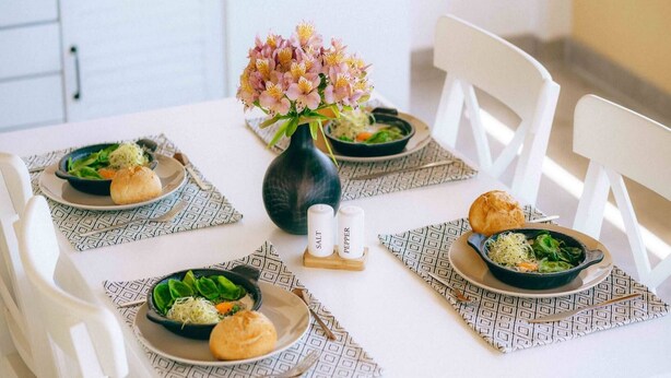 A dining table set with plates of food, salt and pepper shakers, and a vase of flowers.