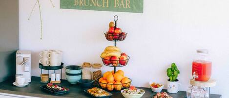 A brunch bar setup with a sign reading "Garden Boutique BRUNCH BAR". There are various food items and drinks displayed on the counter, including fruits, pastries, and a pitcher of juice.