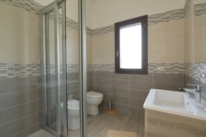 Features a glass-enclosed shower, standalone toilet, and sink in a clean, minimalist design.