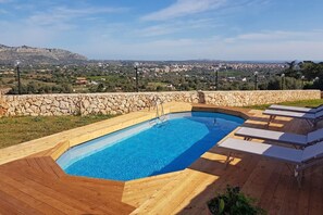 Relax by the pool surrounded by a stone wall and lounge chairs with comfortable cushions.