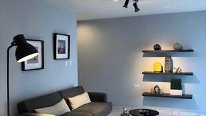 Een moderne woonkamer met een bank, een salontafel, een vloerlamp en wandplanken met decoratieve objecten.