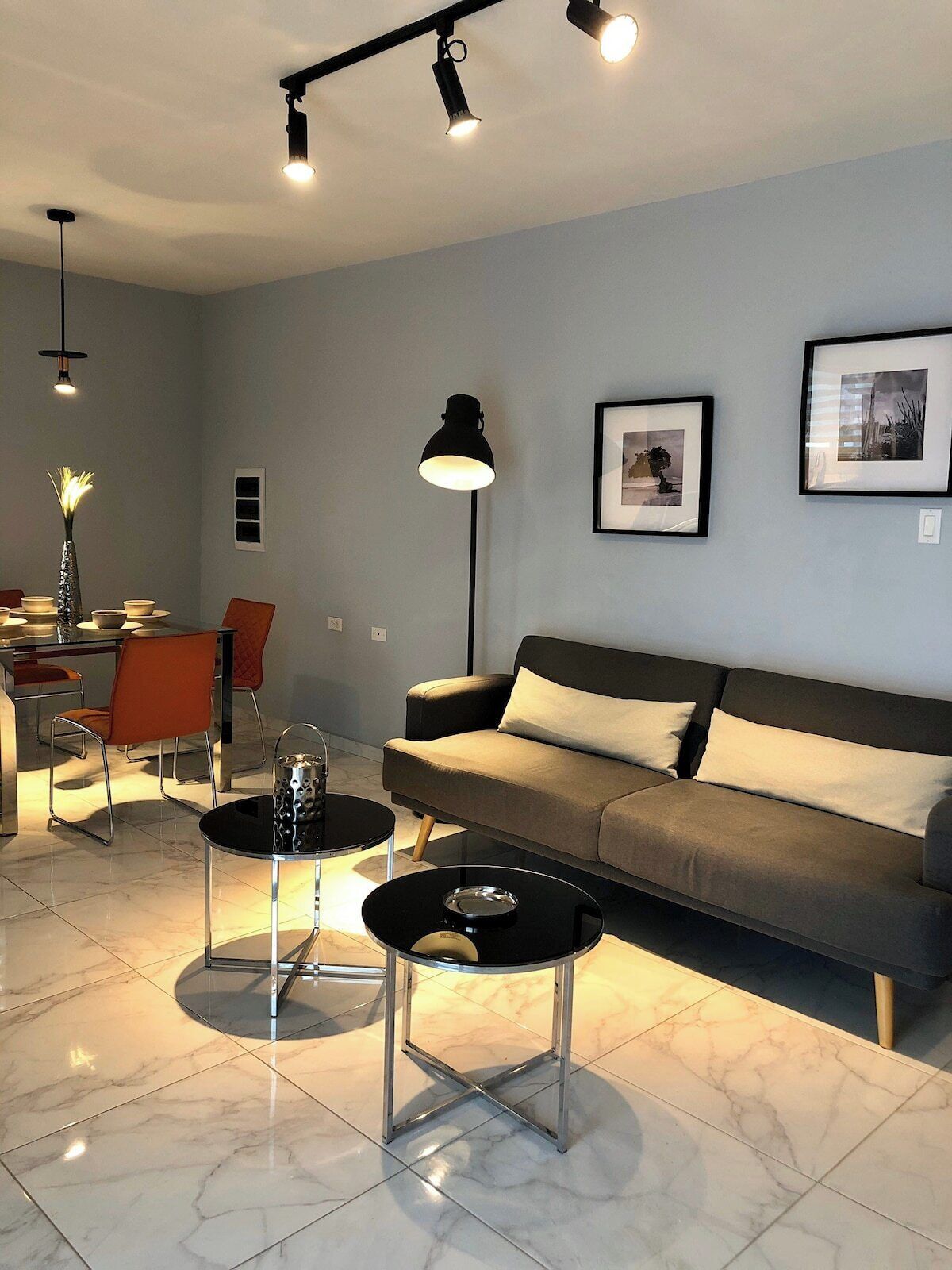 A modern living room with a sofa, two coffee tables, a dining area with chairs, and a floor lamp.