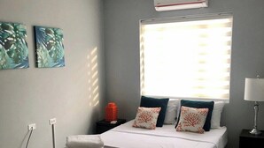 Een slaapkamer met een bed, een raam met zonwering, een airconditioner en kunst aan de muur.