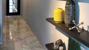 Un pasillo con piso de mármol, una puerta negra al final y estantes con adornos.