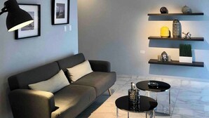 Una sala de estar moderna con un sofá gris, una mesa de centro y una lámpara de pie. Hay estantes con objetos decorativos y un marco de foto en la pared.