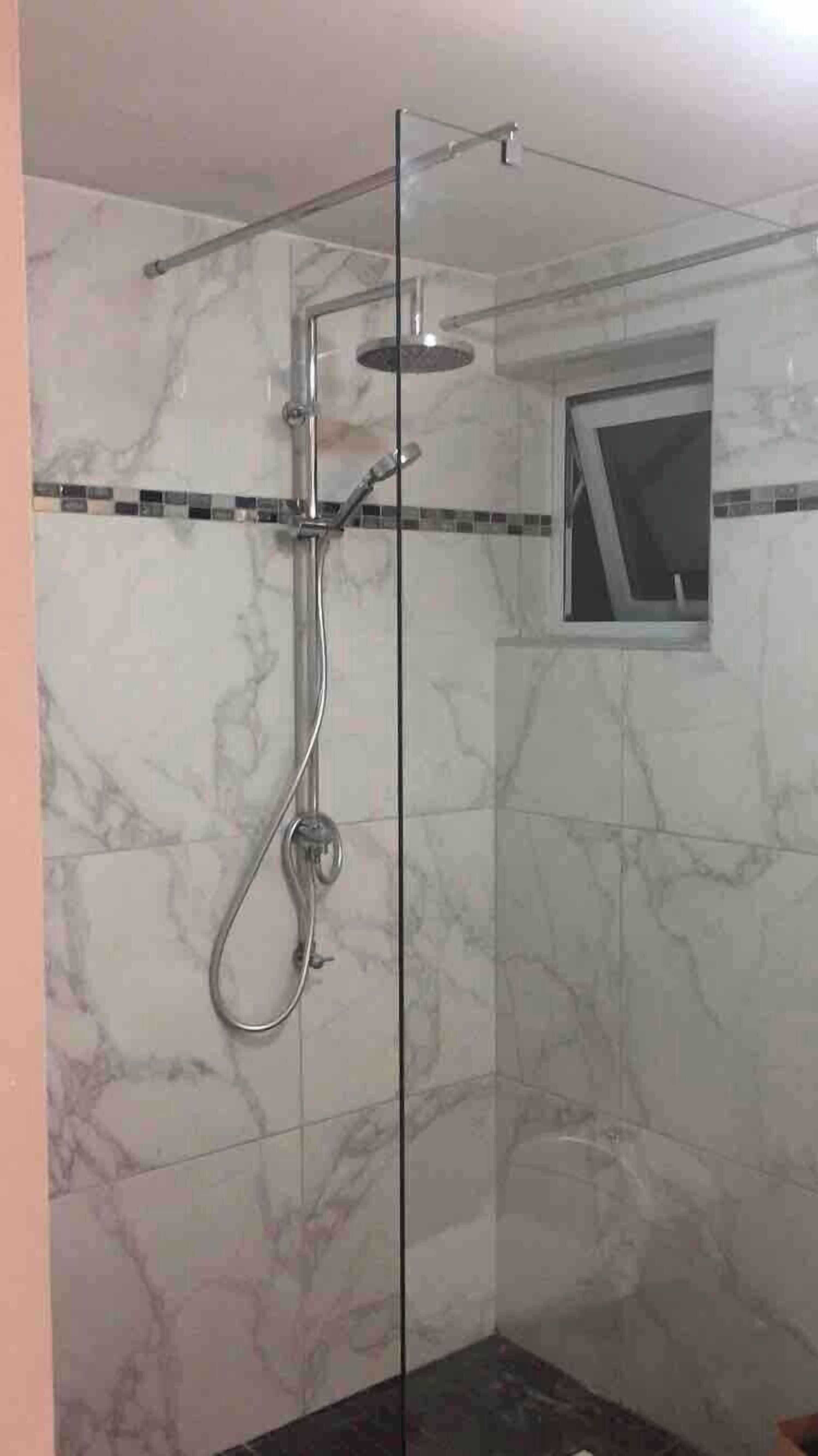 A glass-enclosed shower with a handheld showerhead and a wall-mounted faucet.