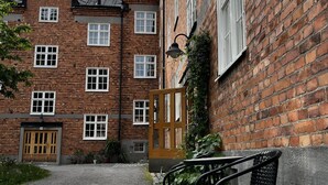 A brick building with multiple windows and a wooden door. There is a gravel path leading to the entrance, and a bench is visible in the foreground. - Lovely Apartment in Stockholm City (Stockholm)