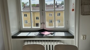 A room with a bay window overlooking a street, featuring a radiator, two chairs, and a small table with a pink mat and a black object. - Lovely Apartment in Stockholm City (Stockholm)