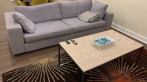 Een moderne woonkamer met een grijze bank, een salontafel met afstandsbedieningen en decoratieve objecten, en een uniek vloerkleed.