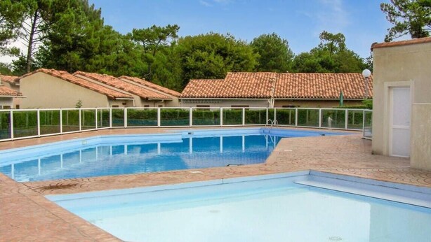 Una piscina rectangular con zona de solárium empaveda, rodeada por una valla blanca.