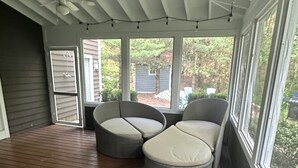 A covered porch with wooden flooring, two grey cushioned seating areas, and a ceiling fan. - Modern Lakeshore Home! 2 minute drive to the beach! Community pool 3 houses away (Union Pier)