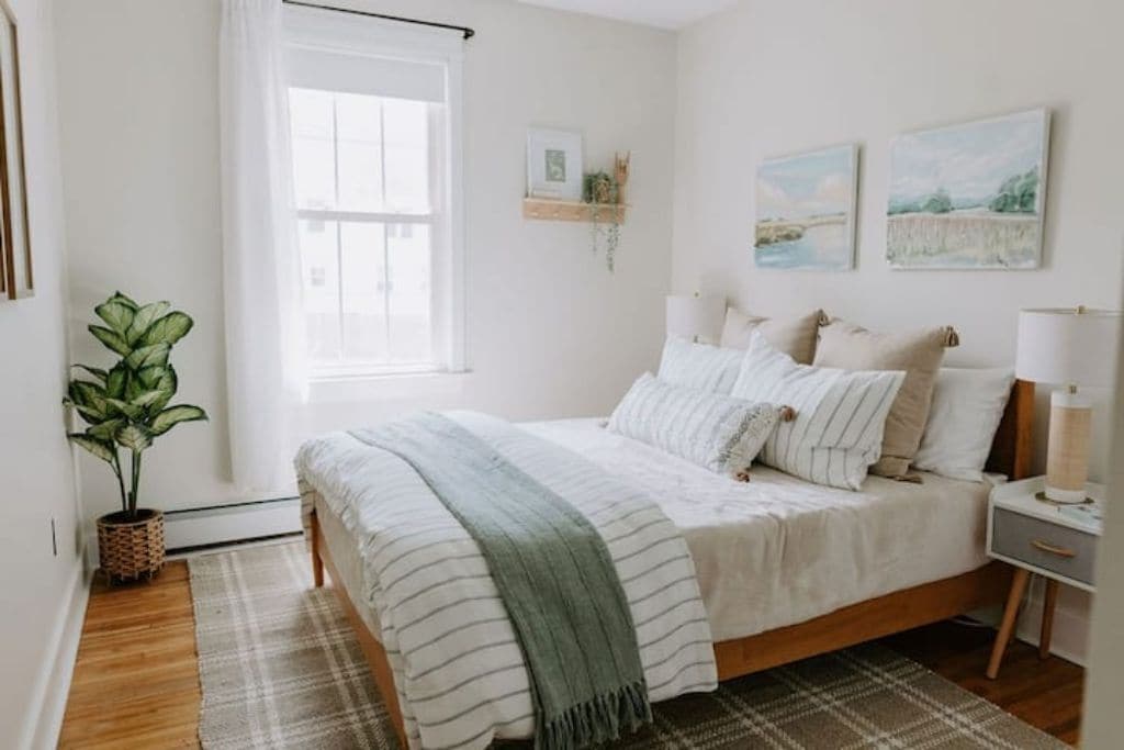 Un dormitorio con cama, mesitas de noche, ventana, planta y decoración en la pared.