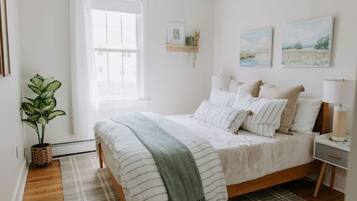Un dormitorio con cama, mesitas de noche, ventana, planta y decoración en la pared.