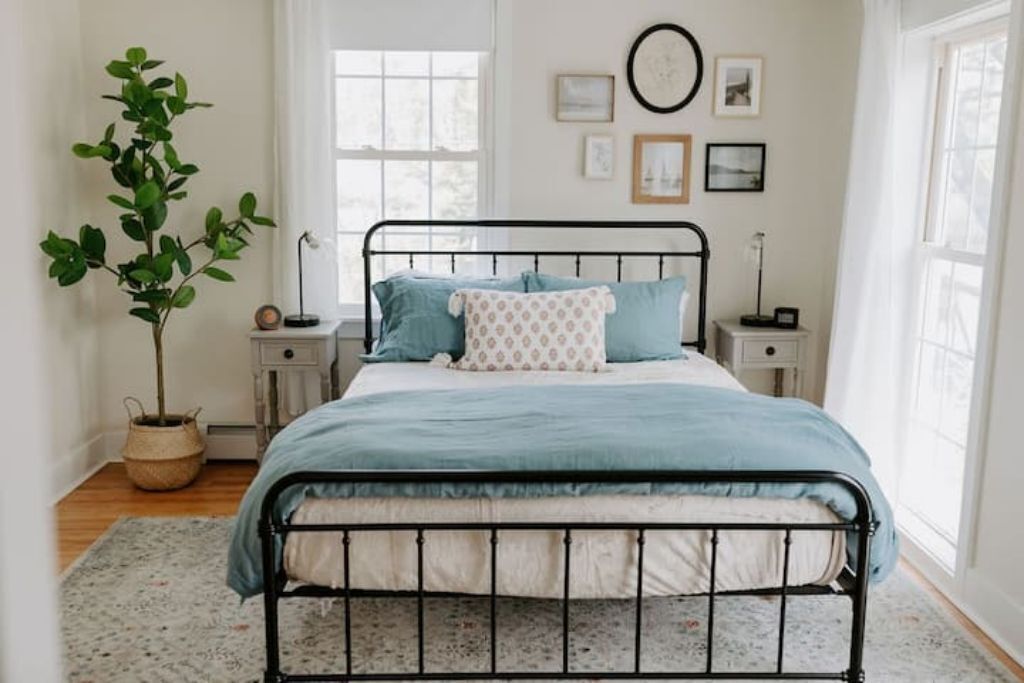 A bedroom with a metal bed frame, a blue bedspread, and a potted plant.