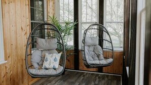 Two hanging chairs with cushions, a wooden floor, and a large window with a view of trees. - Riverside Historic Home near Downtown, Wineries, Hiking (Taylors Falls)