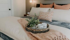 A neatly made bed with a white comforter, a wicker tray with two cups and a plant, and a textured throw blanket. - Riverside Historic Home near Downtown, Wineries, Hiking (Taylors Falls)