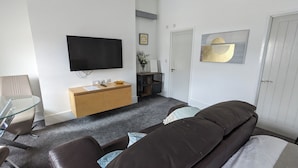 A modern living room with a flat-screen TV, a wooden cabinet, a glass table, and a brown sofa. - Captivating 1-bed Apartment, Merthyr Tydfil - (Merthyr Tydfil)