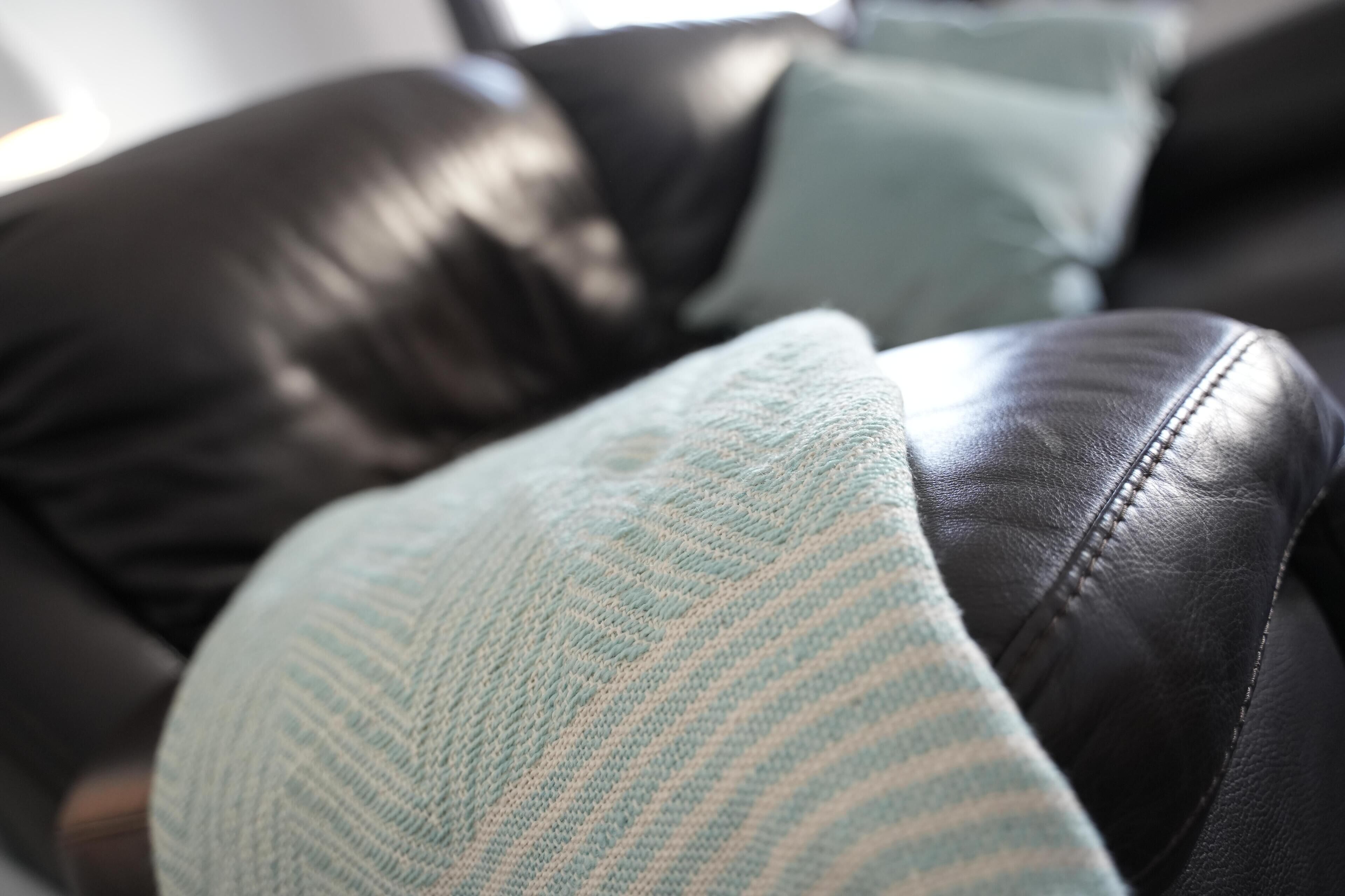 A close-up of a black leather couch with a light blue striped cushion.