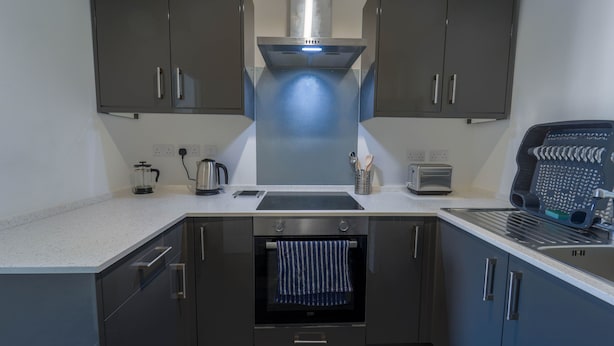 A modern kitchen with grey cabinets, a stainless steel range hood, a built-in oven, and a toaster. - Captivating 1-bed Apartment, Merthyr Tydfil - (Merthyr Tydfil)