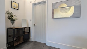 A hallway with a white door, a framed inspirational quote, a vase with plants, a black console table, and a large abstract painting. - Captivating 1-bed Apartment, Merthyr Tydfil - (Merthyr Tydfil)